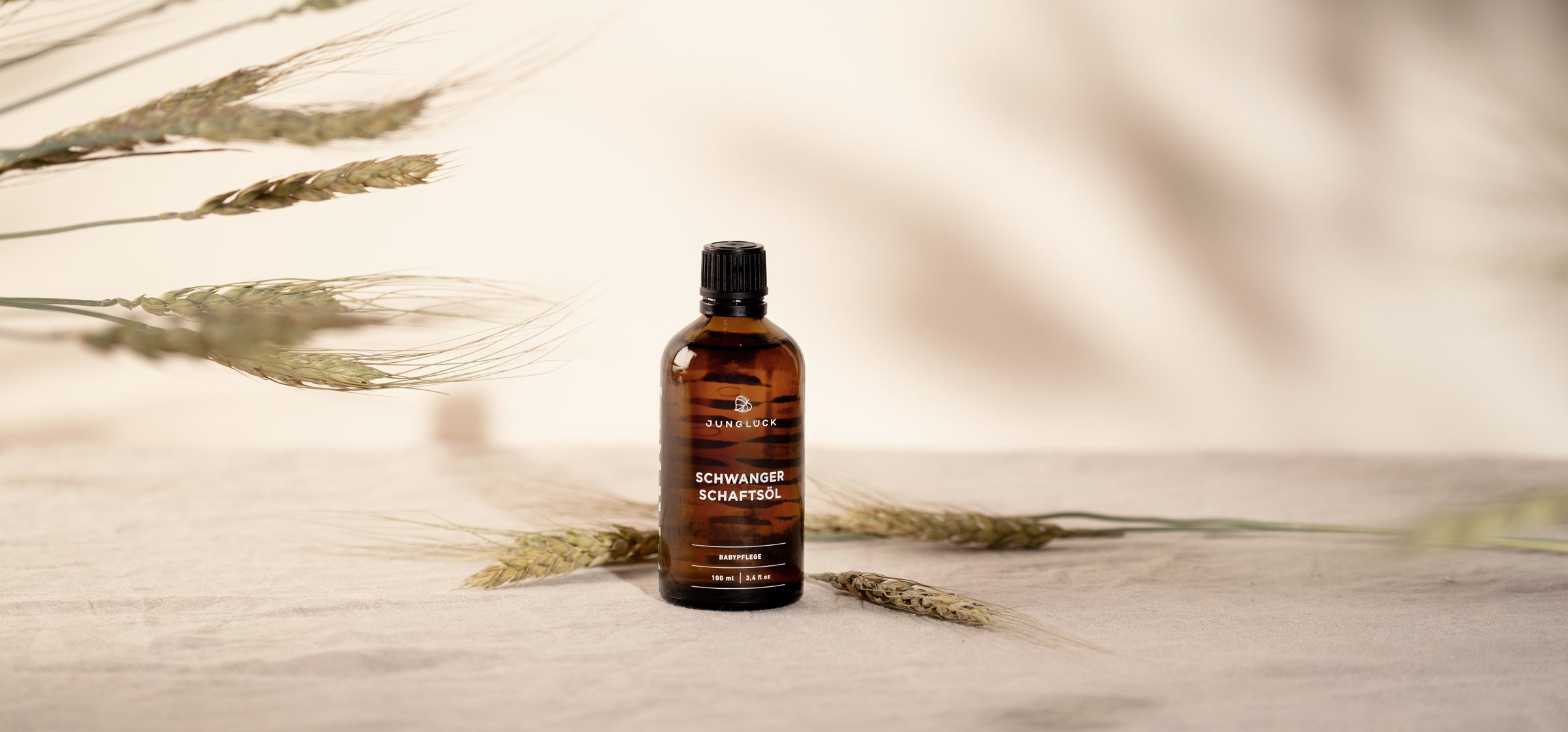 The bottle Pregnancy Oil stands in front of a beige background decorated with wheat stalks.  