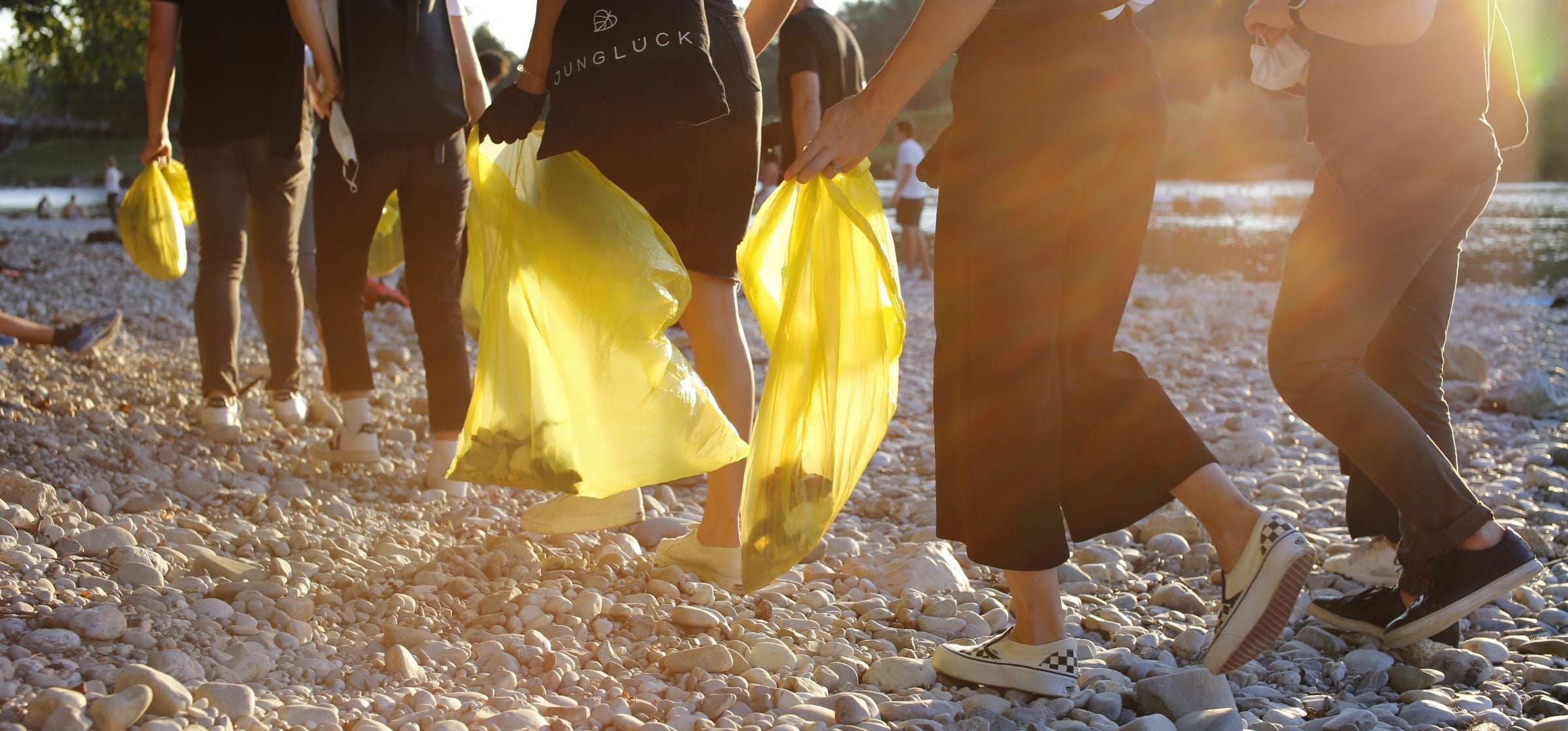 Personen am World Clean Up Day die auf Kies laufen und Mülltüten tragen.