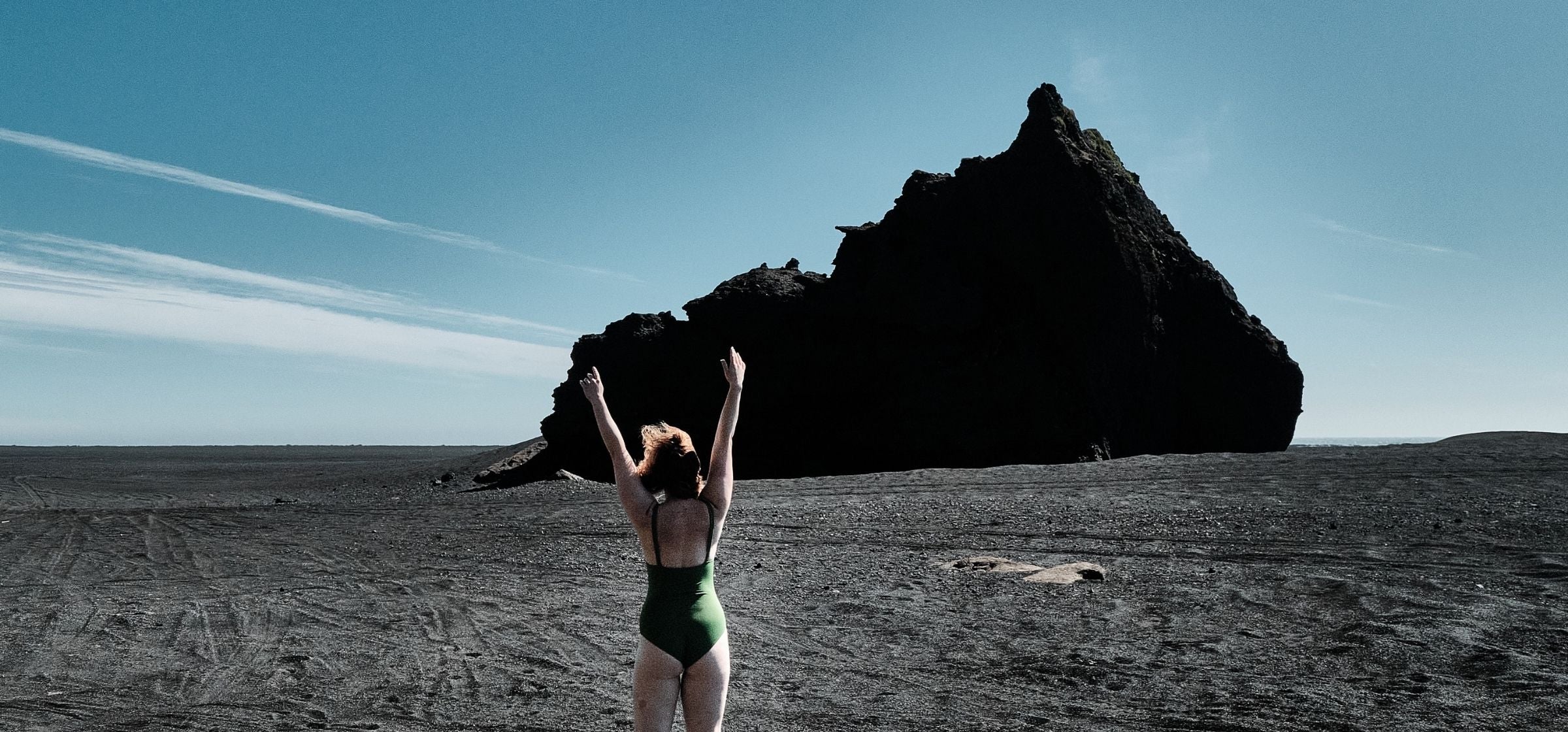 A woman in a green bikini stands in a rocky landscape and raises her arms as a symbol of freedom. 