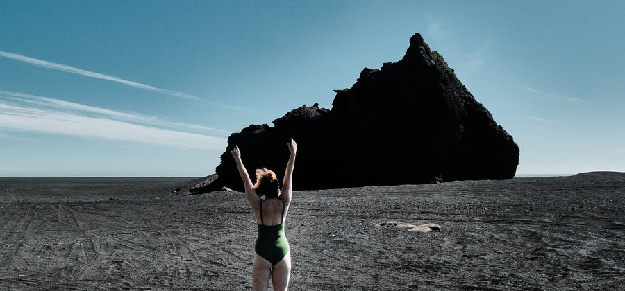 Een vrouw in een groene bikini staat in een rotslandschap en heft haar armen als symbool van vrijheid. 