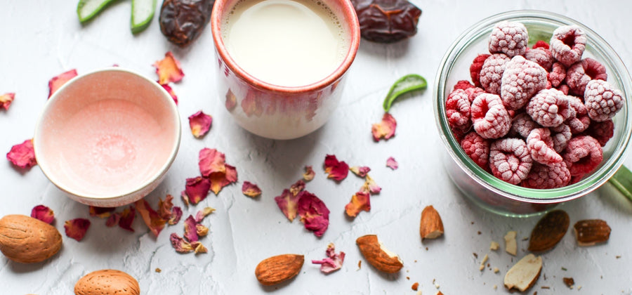 Potete vedere gli ingredienti per un frullato. Lamponi congelati in una ciotola, mandorle, strisce di aloe vera e petali di rosa essiccati.