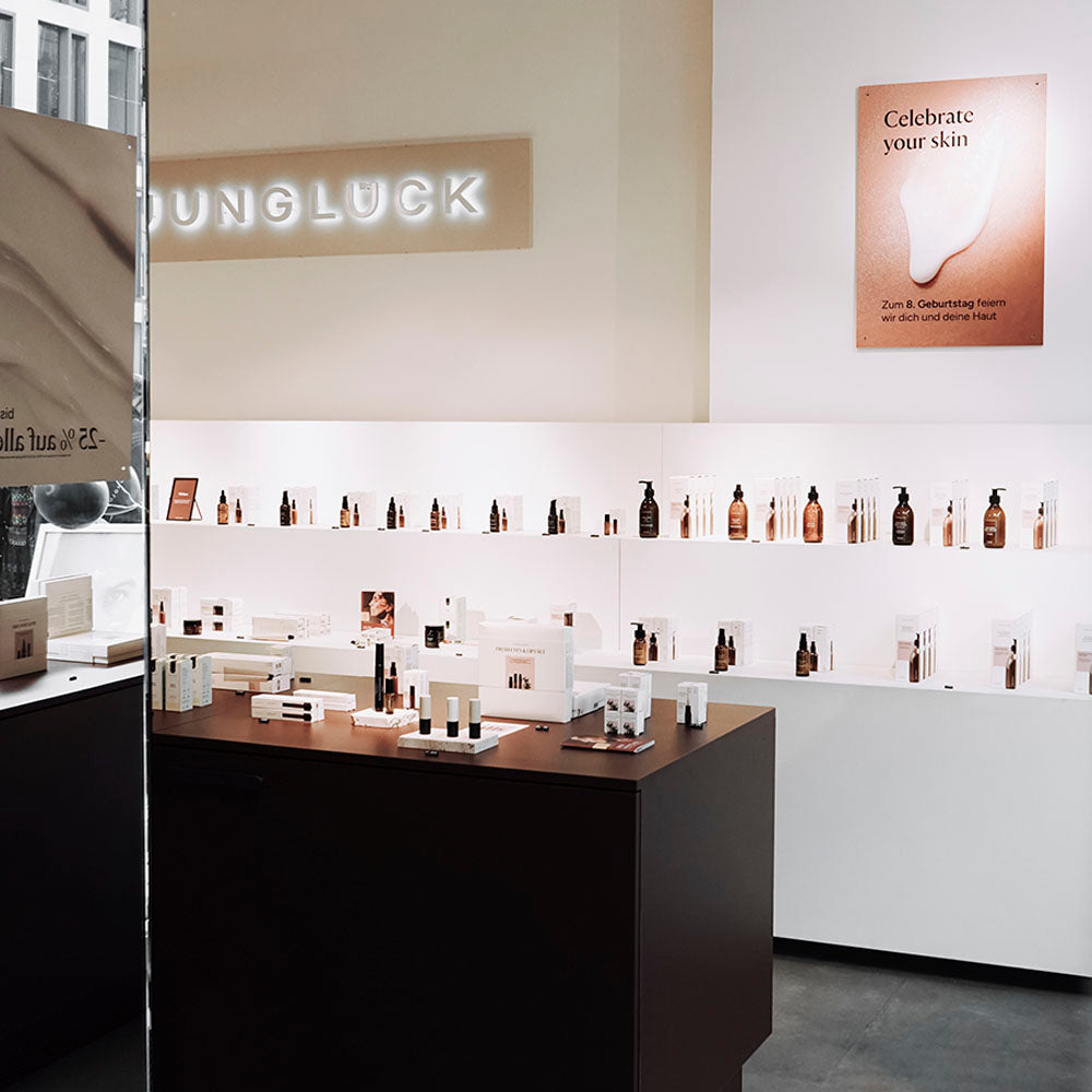 Een kijkje in de JUNGLÜCK-winkel met bruine glazen flessen, verzorgingsproducten en een bord aan de muur met de slogan 'Celebrate your