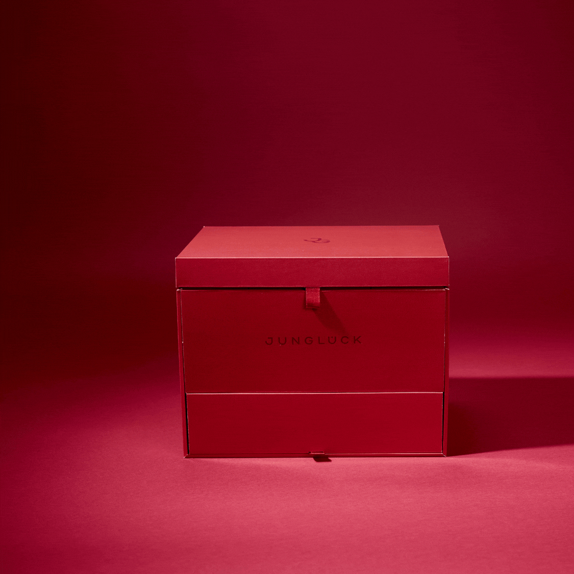 Rote Geschenkbox von JUNGLÜCK auf rotem Hintergrund, elegant und minimalistisch, ohne weitere Details.