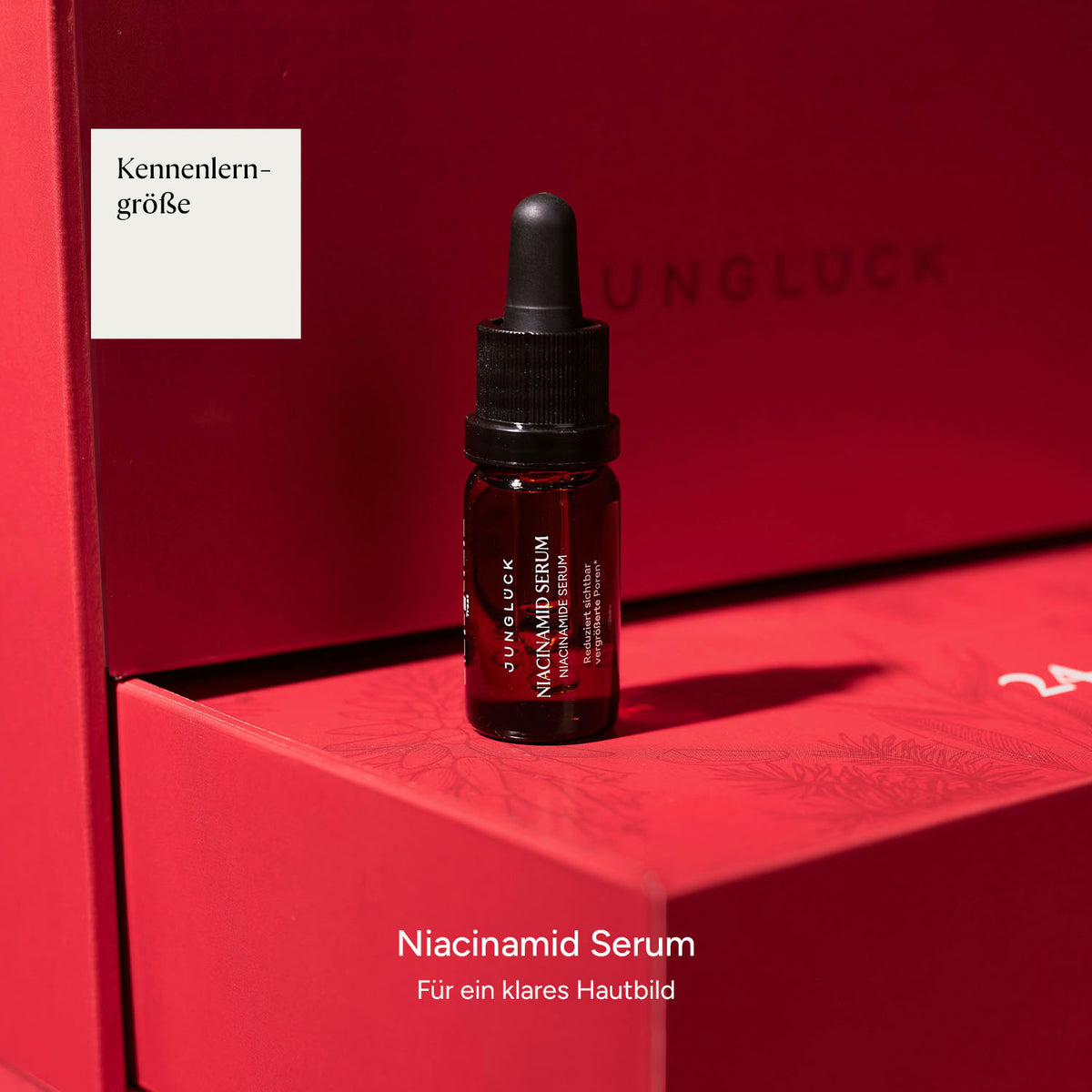 Braunglasflasche mit Niacinamid Serum, platziert auf rotem Karton mit dem Hinweis Kennenlerngröße.